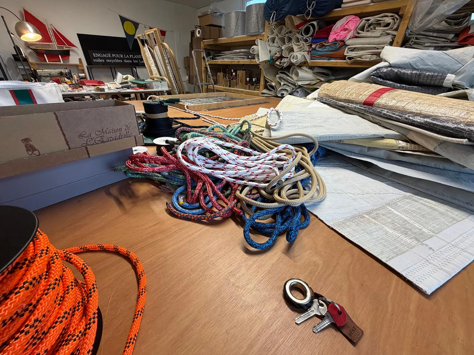 OÈST atelier workbench covered with colourful ropes and folded sails, shelves of rolled sails in the background